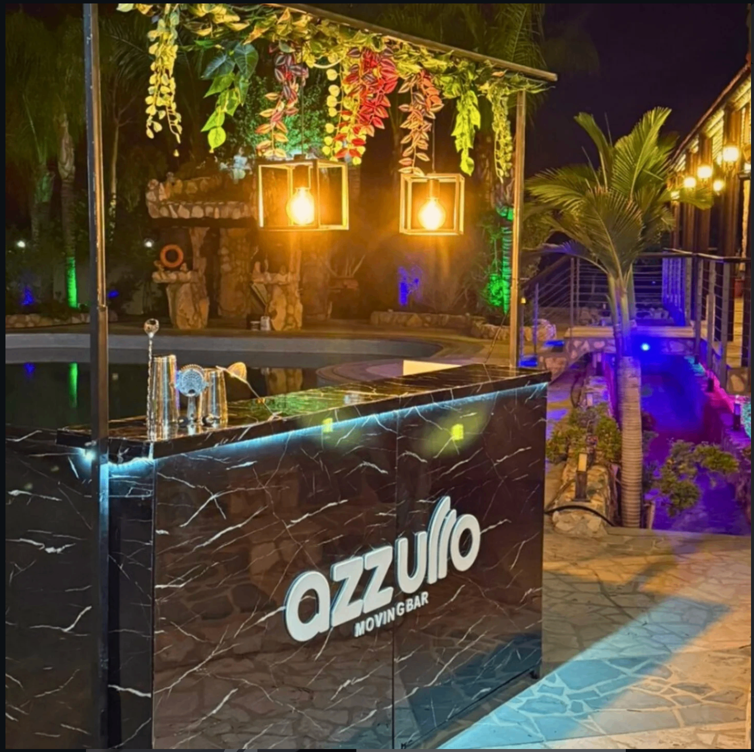 Azzurro Moving Bar black marble mobile cocktail bar set up poolside at a private villa in Cyprus with warm Edison lanterns and tropical greenery
